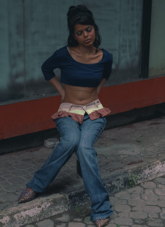 Woman in a blue top and jeans sitting on a curb with a blurred background