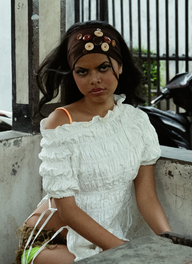 Woman in a white off-shoulder dress sitting outdoors with brown buttoned headband
