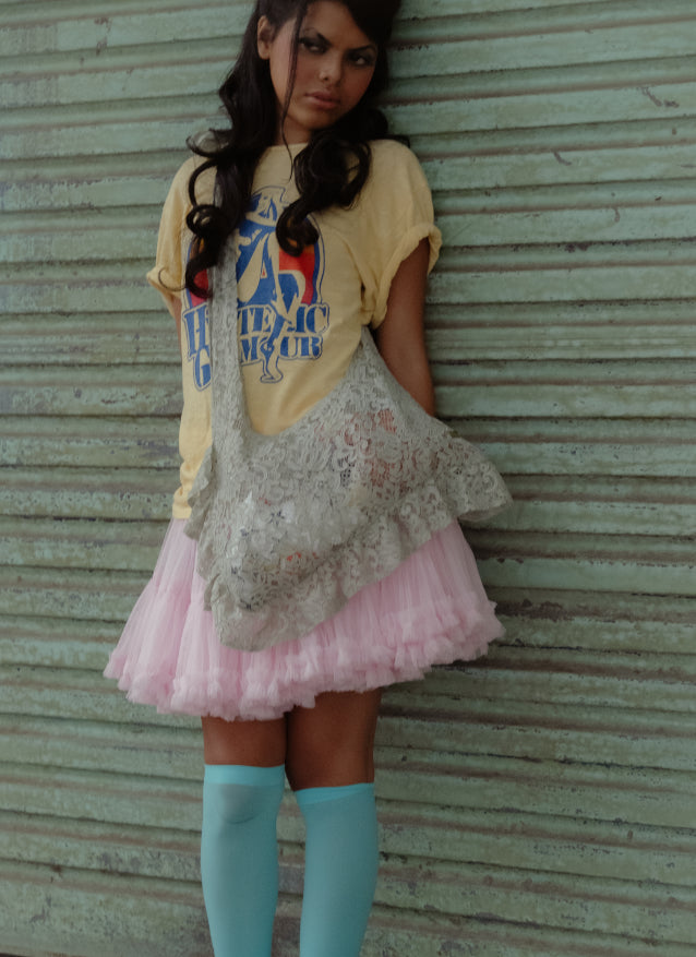 Woman wearing a yellow graphic t-shirt, pink skirt, and blue knee-high socks carrying sling lace mint green bag.
