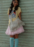 Woman wearing a yellow graphic t-shirt, pink skirt, and blue knee-high socks carrying sling lace mint green bag.