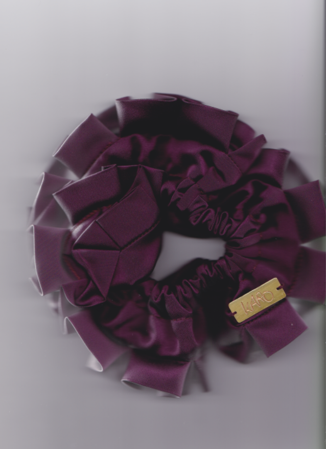Purple scrunchie with a gold tag on a light gray background