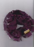 Purple scrunchie with a gold tag on a light gray background